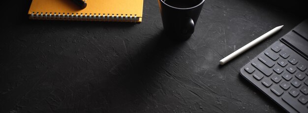 Stijlvolle werkruimte met koffiekopje, notebook, stylus, digitale tablet op zwarte tafel