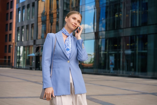 Stijlvolle zakenvrouw in een blauw jasje met een telefoon in de hand staat in het zakencentrum