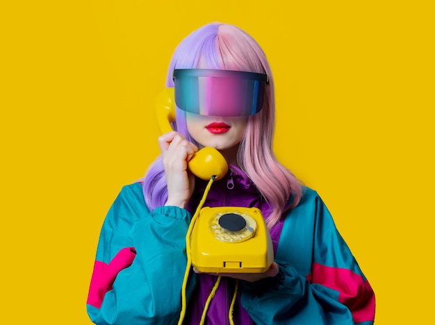 Foto stijlvrouw in vr-bril en jaren 90-sportpak met telefoon op gele achtergrond