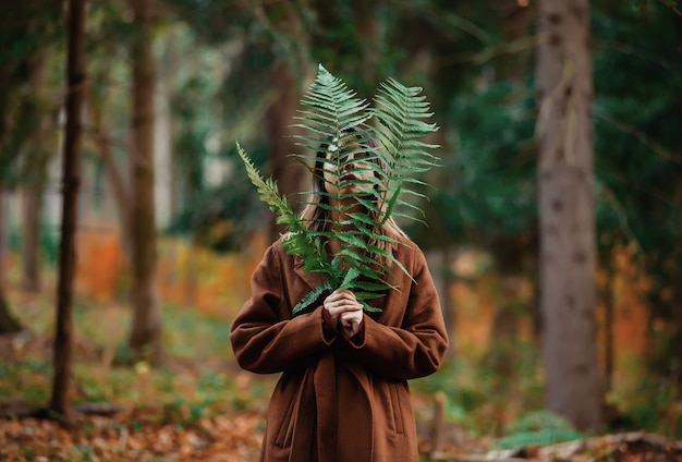 Stijlvrouw met varentak in een bos van de de herfsttijd