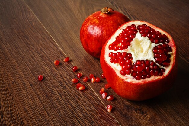 Stil life - red whole and cutted pomegranate fruits and scattered seeds on a dark wooden tabletop