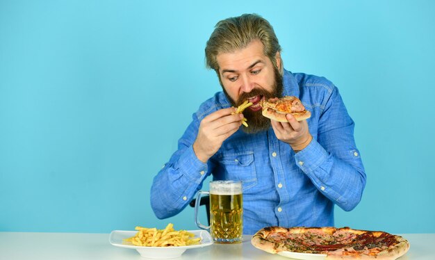 まだ空腹のビールと食べ物パブでの夕食空腹の男がピザのフレンチフライを食べてビールを飲むピッツェリアレストラン陽気な男ひげを生やしたヒップスターがピザを食べるピザパーティーのコンセプト食欲をそそる