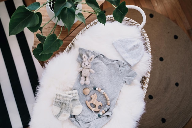 Still life background of cute baby products changing basket with baby bodysuit newborn clothes knitted rabbit and wooden toy Minimalist style photography of baby shower pregnancy announcement