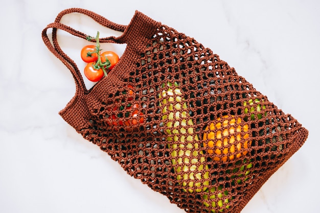 Still life of biodegradable shopping bag with raw vegetables on marble background