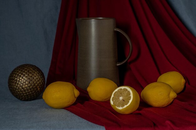 Still life on a blue background with red draperies, lemons, jug