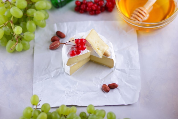 Still life of cheese fruit and a green bottle on a blurred background Camembert French cream cheese made from cow's milk served with honey and fruit on white parchment Closeup