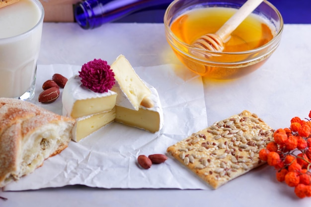 Still life of cheese honey walnuts fruit and a blue bottle on a blurred background Food for a healthy and tasty snack on a white parchment Closeup