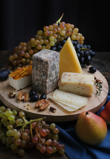 Still life of Cheese plate assortment. Fruits, knife and nuts with different cheese on wooden board