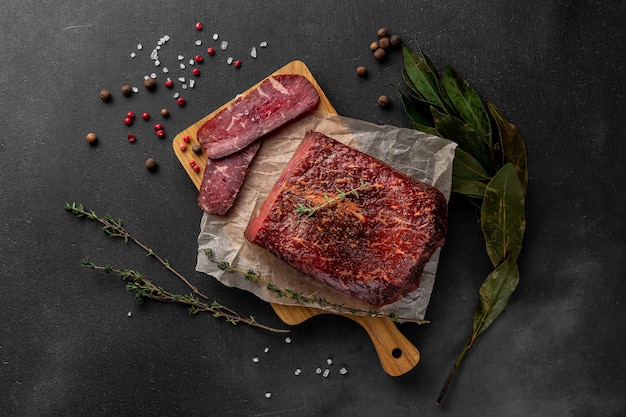 Still life composition with a piece of red smoked dry ham on a wooden cutting board, top view