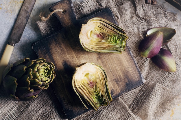 Photo still life composition with raw organic artichoke on vintage wooden board