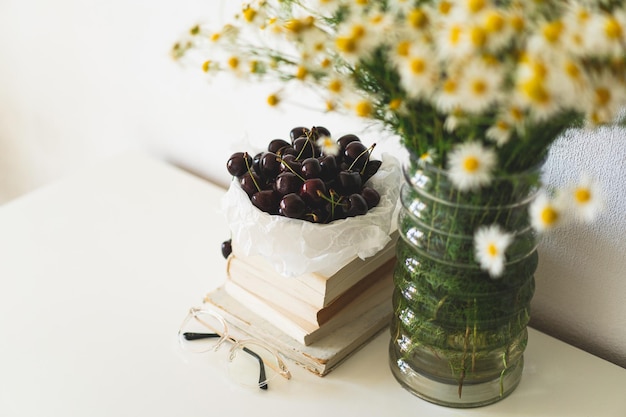 거실 홈 인테리어의 정물 세부 정보 책 체리와 카모마일 꽃이 있는 꽃병 읽기 및 휴식 아늑한 봄 개념