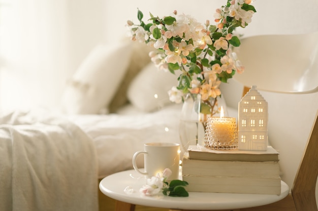 Still life details in home interior of living room. book, hot\
cup tea, candle and vase with apple spring flowers. read and\
rest