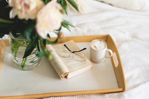 Still life details in home interior of living room Open book with glasses cup coffee and bouquet white pink peonies flowers Read and rest Cozy home