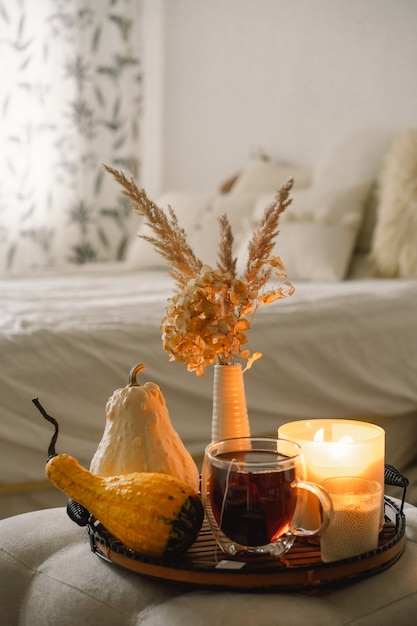 Still life details in home interior of living room. Pumpkin and cup of tea with candles on a serving tray. Cozy autumn