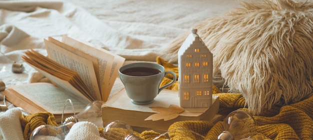 Still life details in home interior of living room. Sweaters and cup of tea with a candle house and autumn decor on the books. Read, Rest. Cozy autumn or winter concept.