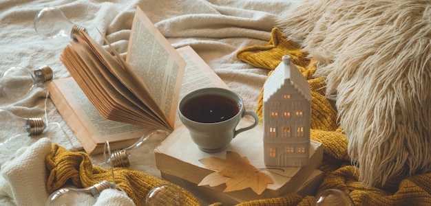リビングルームのインテリアの静物詳細。セーターとキャンドルハウスと本の秋の装飾とお茶のカップ。読んで、休憩。居心地の良い秋や冬のコンセプトです。