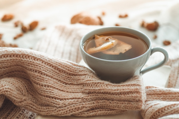 Still life details in home interior of living room. Sweaters and cup of tea with a cone,  nuts and autumn decor on the books. Read, Rest. Cozy autumn or winter concept.