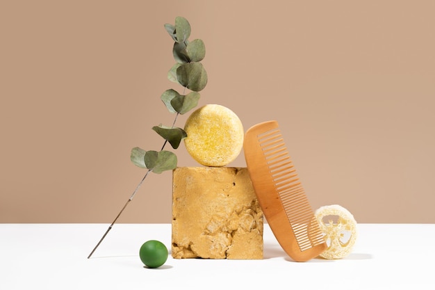 Still life modern composition solid shampoo bar and natural\
materials an idea balance wooden comb luffa sponge eucalyptus on a\
beige background plastic free zero waste low water ingredients