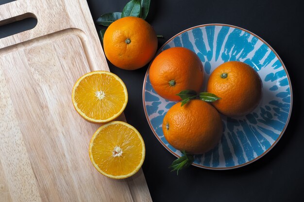 Still life of oranges on wooden cutting board with blue plate, black background