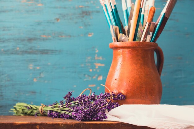 Still life of paint brushes in clay jug an lavender flower on vintage turquoise background