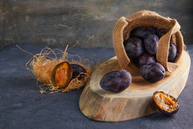 Still life of plums in a bag and hay on a wooden stand