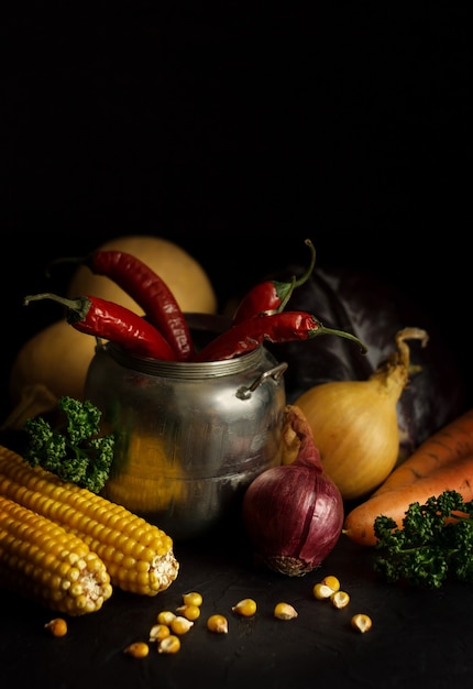 Still life of raw vegetables. Hot peppers, onion and corn on a dark background