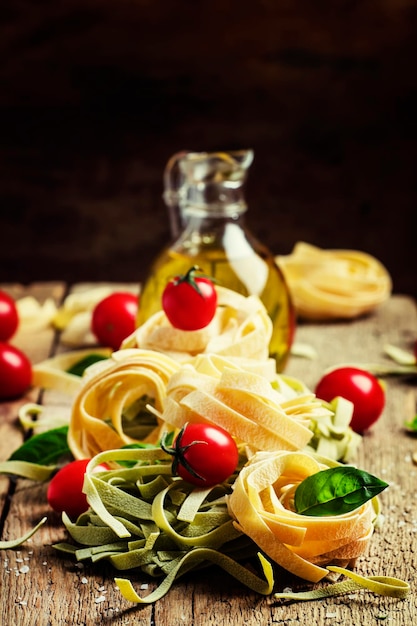 Still life in rustic style Nest of pasta with cherry tomatoes olive oil and green basil Vintage wooden background selective focus shallow depth of field