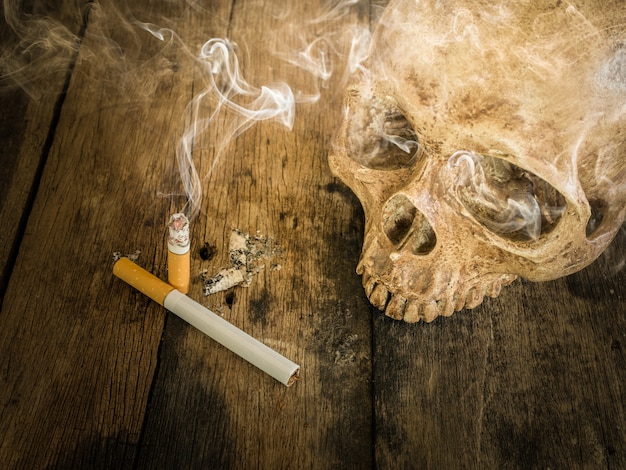 Still life skull and cigarette burned with smoke on wood.