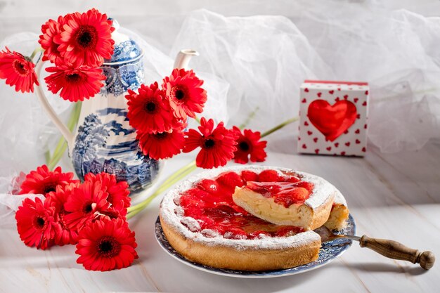 Still life strawberry pie with pudding and a kettle with a bouquet of red gerberas valentines gift