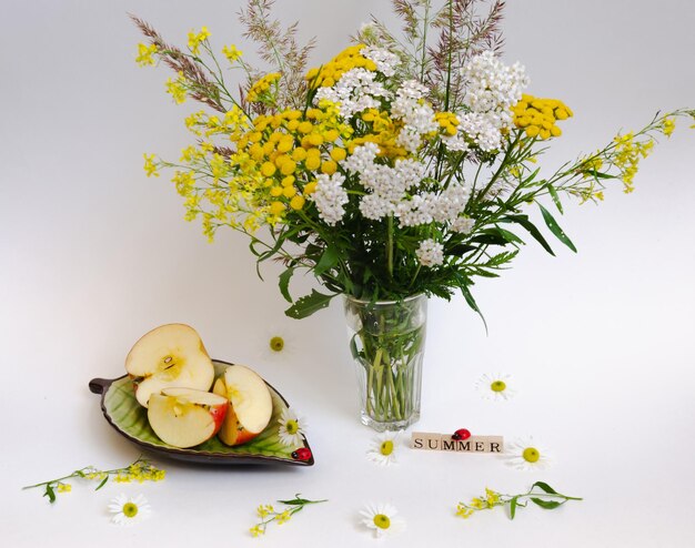 Still life of wildflowers and an apple on a saucer all on a light background