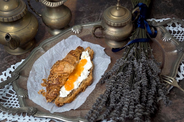 Фото Натюрморт с круассаном, наполненным свежим сыром и абрикосовым джемом, старый кофейный сервиз