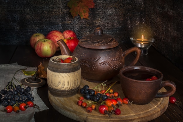 Still life with autumn tea from a dogrose and hawthorn and a clay teapot on a wooden background.