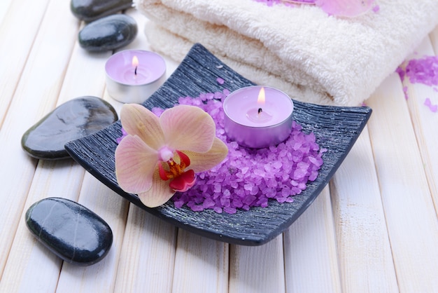 Still life with beautiful blooming orchid flower, towel and bowl with sea salt, on color wooden background