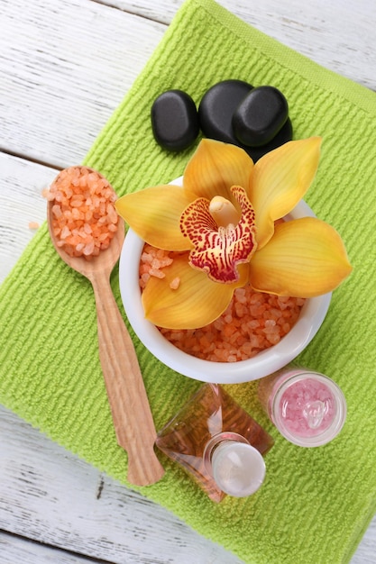 Still life with beautiful blooming orchid flower towel and sea salt in bowl on color wooden background