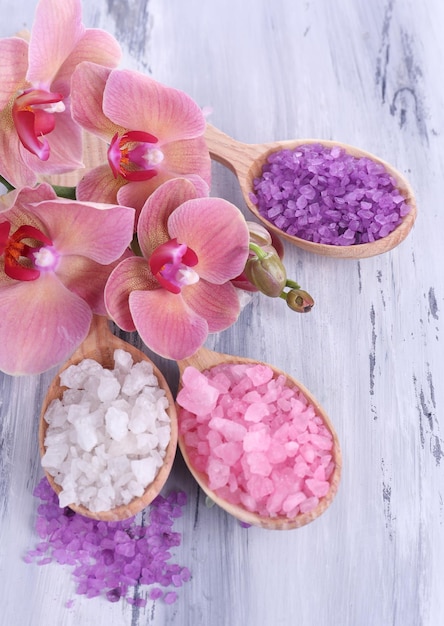 Still life with beautiful blooming orchid flower and wooden spoons with sea salt on color wooden background