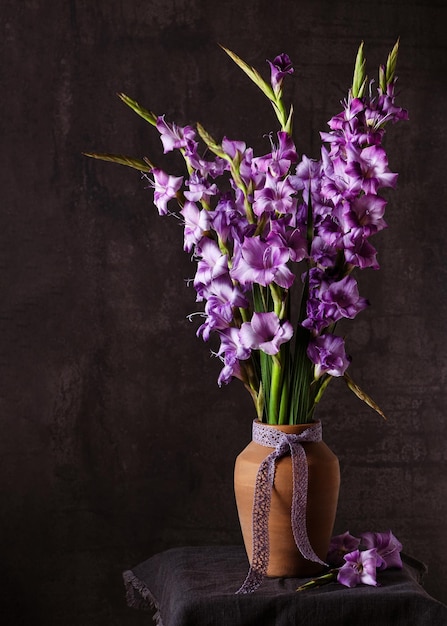 Still life with beautiful bouquet of lila, purple gladioli flowers in ceramic vase