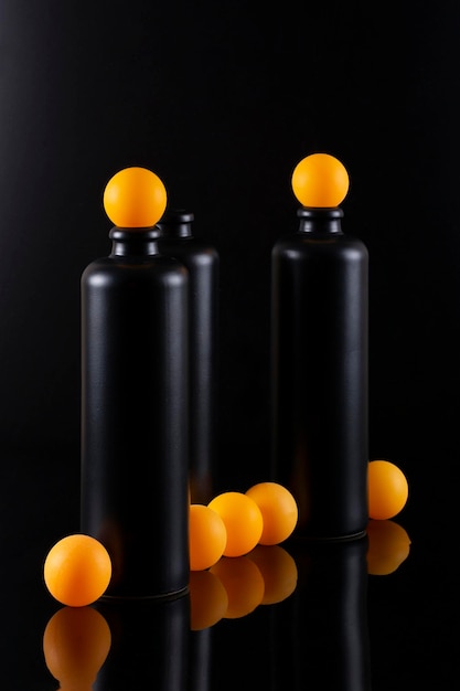 Still life with black bottles and orange balls on a black background