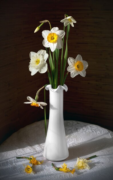 Still life with a bouquet of daffodils in white vase on a round table with a white tablecloth.