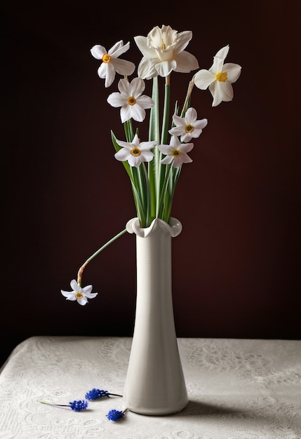 Still life with a bouquet of daffodils in white vase and scattered hyacinths on a round table with a white tablecloth.