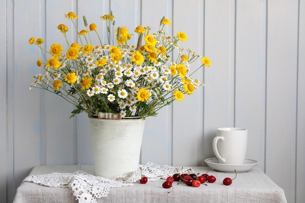 Still life with a bouquet of daisies and ripe cherry berries on the table in bright cottage interior