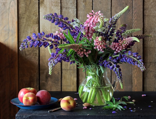 Still life with a bouquet of lupine in the clear pitcher, Apple and peaches