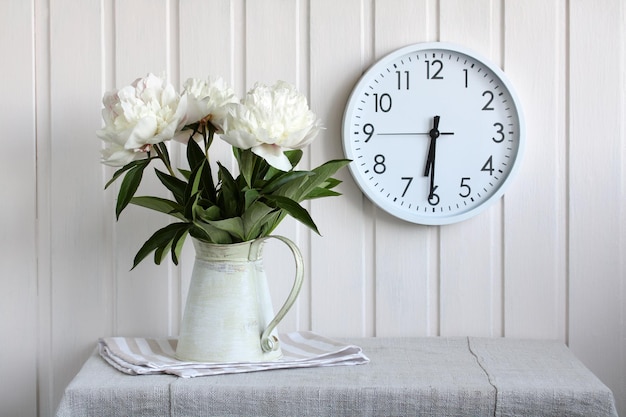Still life with a bouquet of white peonies and a clock on a wooden wall