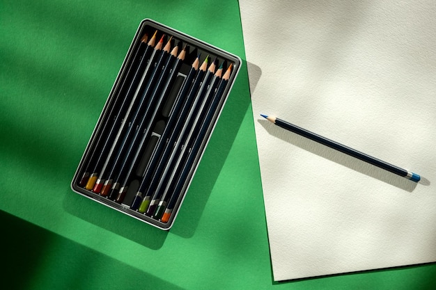 Still life with a box of pencils a sheet of paper and a pencil on a green background