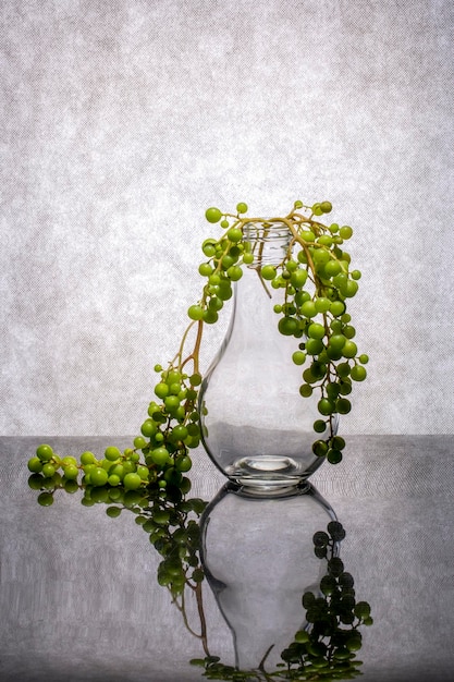 Photo still life with a branch of green grapes and a glass vase