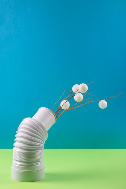 Still life with a branch and white balls in a white vase on a colored background