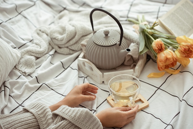 一杯のお茶、ティーポット、ベッドの中でチューリップの花束のある静物がクローズアップ。週末と春の朝のコンセプト。