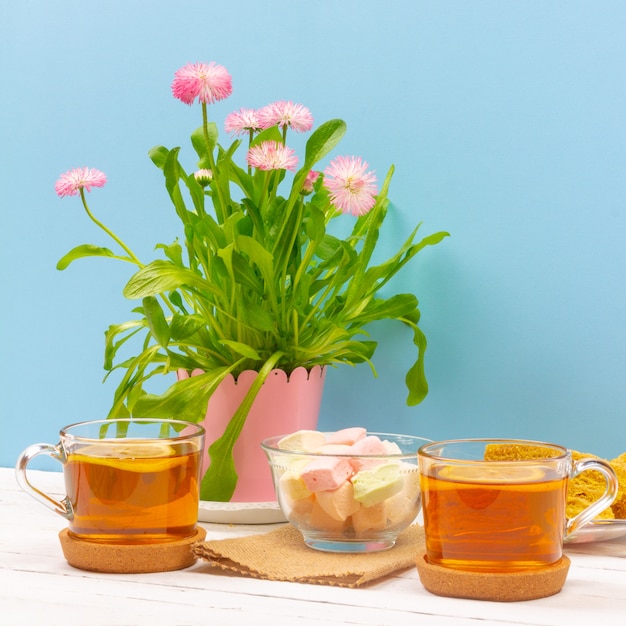 Photo still life with cups of tea, pieces of cake, bouquet of pink flowers in a pink pot, marshmallow