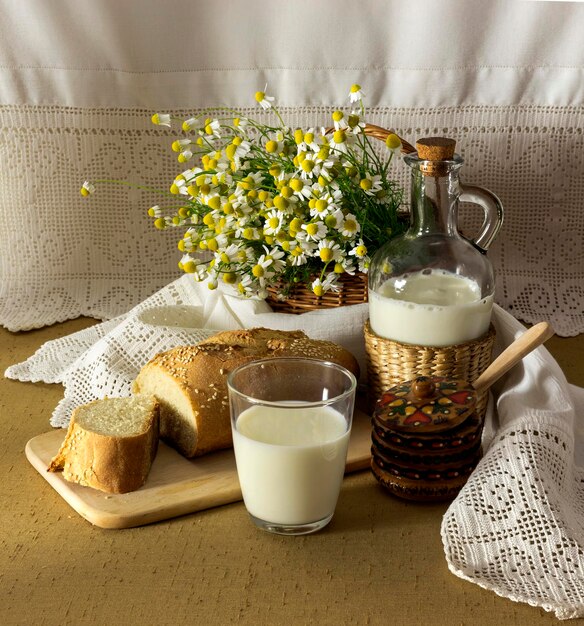 Натюрморт с целебными ромашками, молоком и хлебом на столе крупным планом