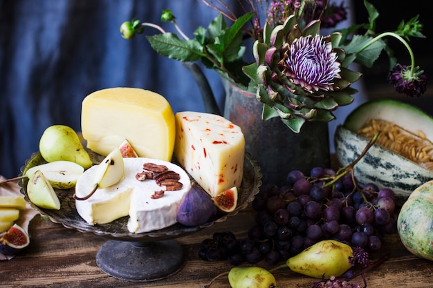 Still life with different cheese, fresh fruit, and garden flowers