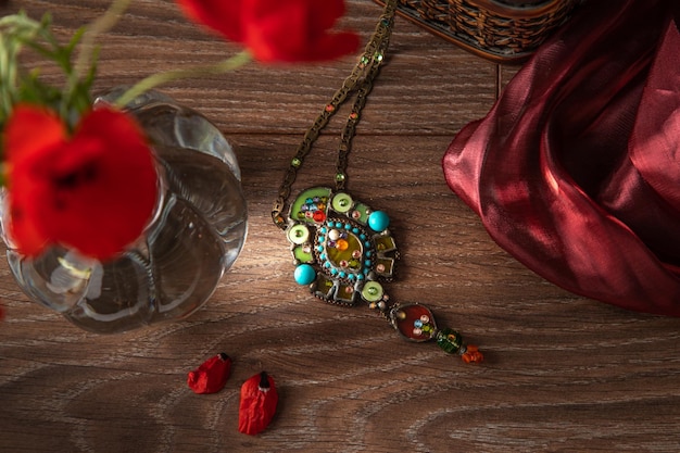 Still life with a fan a bouquet of poppies and Jewelry pendant with semiprecious stones Rustic style